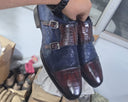 Hand holding a pair of blue and brown dress shoes in an indoor setting.