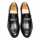 A pair of black leather penny loafers with silver-tone metal hardware, displayed on wooden shoe trees against a white background.