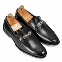 A pair of men's black leather penny loafers with silver-tone metal hardware, displayed on wooden shoe trees against a clean white background.
