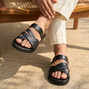 Person wearing black sandals on a stone floor with a wooden bench in the background