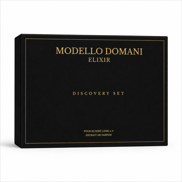 A black rectangular product box with elegant gold lettering reading 'MODELLO DOMANI ELIXIR' and 'DISCOVERY SET' on a clean white background. Men and women perfume fragrances. Unisex perfumes. Gifting set. 