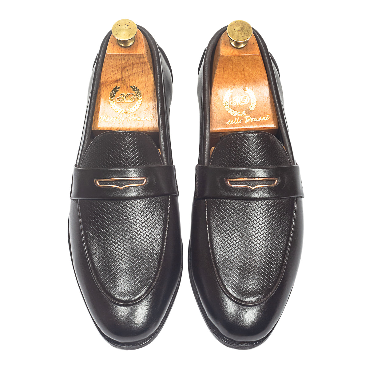 Brown leather loafers worn with gray pants on a wooden floor.