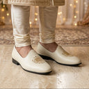 White embroidered shoes worn with a traditional outfit in a decorated room.