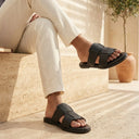 Person wearing black sandals sitting on a stone bench with a neutral background