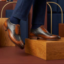 Brown leather dress shoes worn with navy pants on a wooden platform.