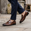 Brown loafers worn with navy pants on a stone pavement.