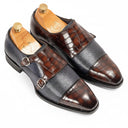 A pair of men's double-strap loafers in mixed leather textures, featuring a dark brown crocodile-embossed toe, a dark blue-gray textured strap, and a medium brown crocodile-embossed side panel. The shoes are displayed on wooden shoe trees against a clean white background.