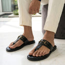 Black sandals with gold buckles worn by a person on a light-colored floor.