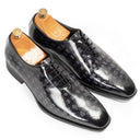 A pair of men's dress shoes with a glossy black crocodile-embossed leather finish, displayed on wooden shoe trees against a clean white background.