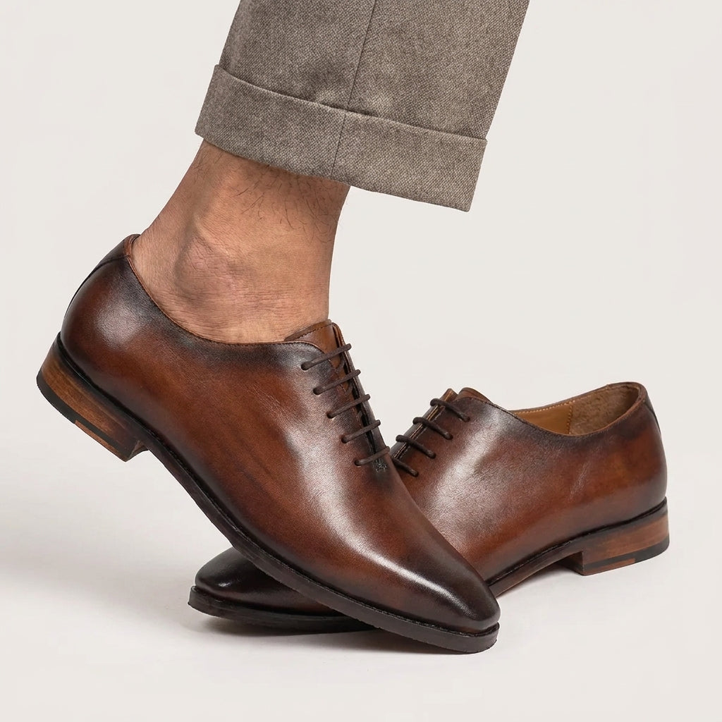 Brown leather dress shoes worn with gray pants on a light background