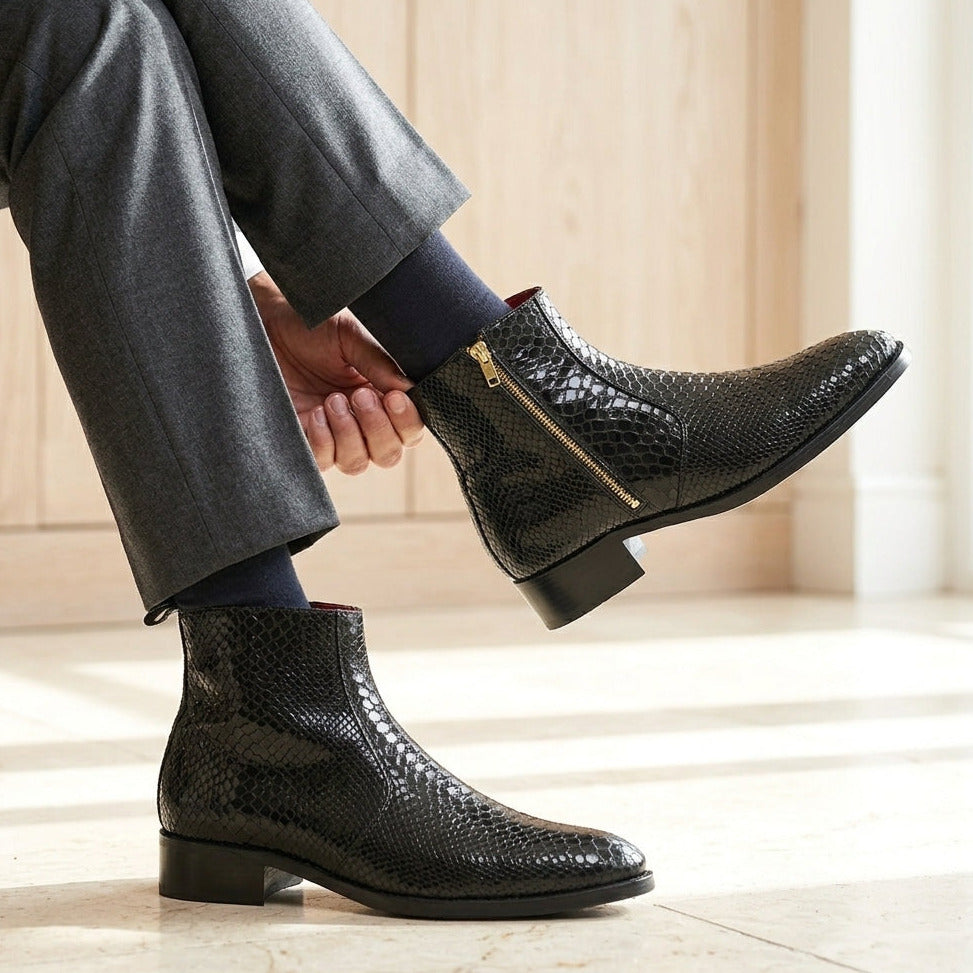 Black textured ankle boots worn with gray pants on a light wooden floor.