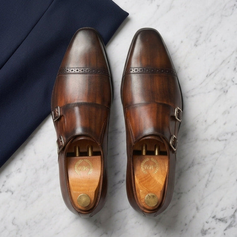 Pair of brown leather shoes with gold buckles on a marble surface.