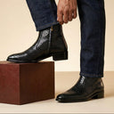 Black leather boots worn with blue jeans on a beige background