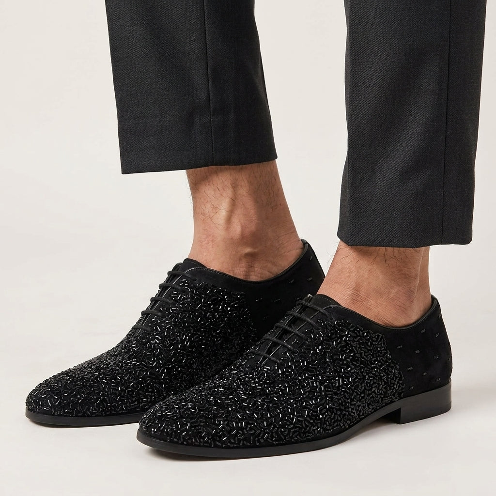 Black textured dress shoes worn with black pants on a light background