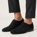 Black textured dress shoes worn with black pants on a light background
