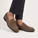 Brown loafers worn with black pants on a light gray background