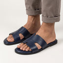 Navy sandals worn with rolled-up beige pants on a light gray background