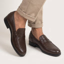 Brown leather loafers worn with beige pants on a light background