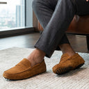 Person wearing brown loafers sitting on a chair with a cityscape view.