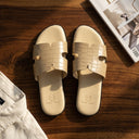 Beige crocodile-patterned slides on a wooden surface with a magazine in the background.