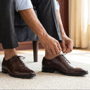 Person tying brown dress shoes indoors