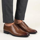 Brown dress shoes worn with gray pants on a neutral background