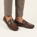 Brown loafers worn with beige pants on a light background