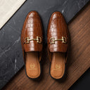 Brown leather loafers with gold buckles on a dark surface