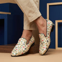 Floral-patterned loafers worn with beige pants against a blue and brown background