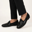 Black sequin loafers worn with black pants on a white background