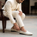 Man in a white suit adjusting his white loafers on a wooden floor.