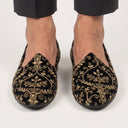 Black loafers with gold embroidery worn by a person on a white background