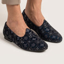 Navy blue embroidered shoes worn by a person on a light gray background