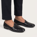 Black woven loafers worn with black pants on a light gray background