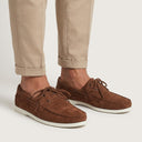 Brown suede shoes worn with beige pants on a white background