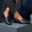 Person wearing black woven loafers with a dark background