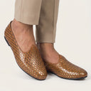 Brown perforated loafers worn with beige pants on a light background
