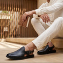Man in white traditional outfit wearing black shoes sitting on a wooden floor.
