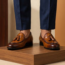 Brown loafers worn with navy pants on a wooden platform
