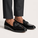 Black patent leather loafers worn with dark trousers on a light background