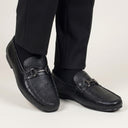 Black leather loafers worn with black pants on a light gray background