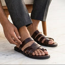 Man sitting outdoors adjusting his sandals with a blurred background
