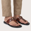 Brown sandals with gold buckles worn with beige pants on a white background