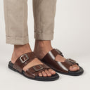 Brown sandals with buckles worn with beige pants on a light gray background