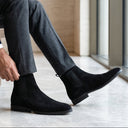 Man sitting on a bench wearing black Chelsea boots indoors.