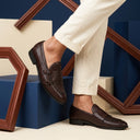 Brown loafers worn with white pants against a geometrically patterned background