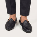 Black woven shoes worn with black pants on a light gray background