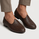 Brown woven loafers worn with beige pants on a light background. hand woven made juttis in leather men