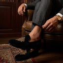 Man in a suit sitting on a leather chair with a bookshelf in the background