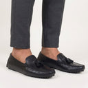 Black loafers with tassels worn with gray pants on a white background